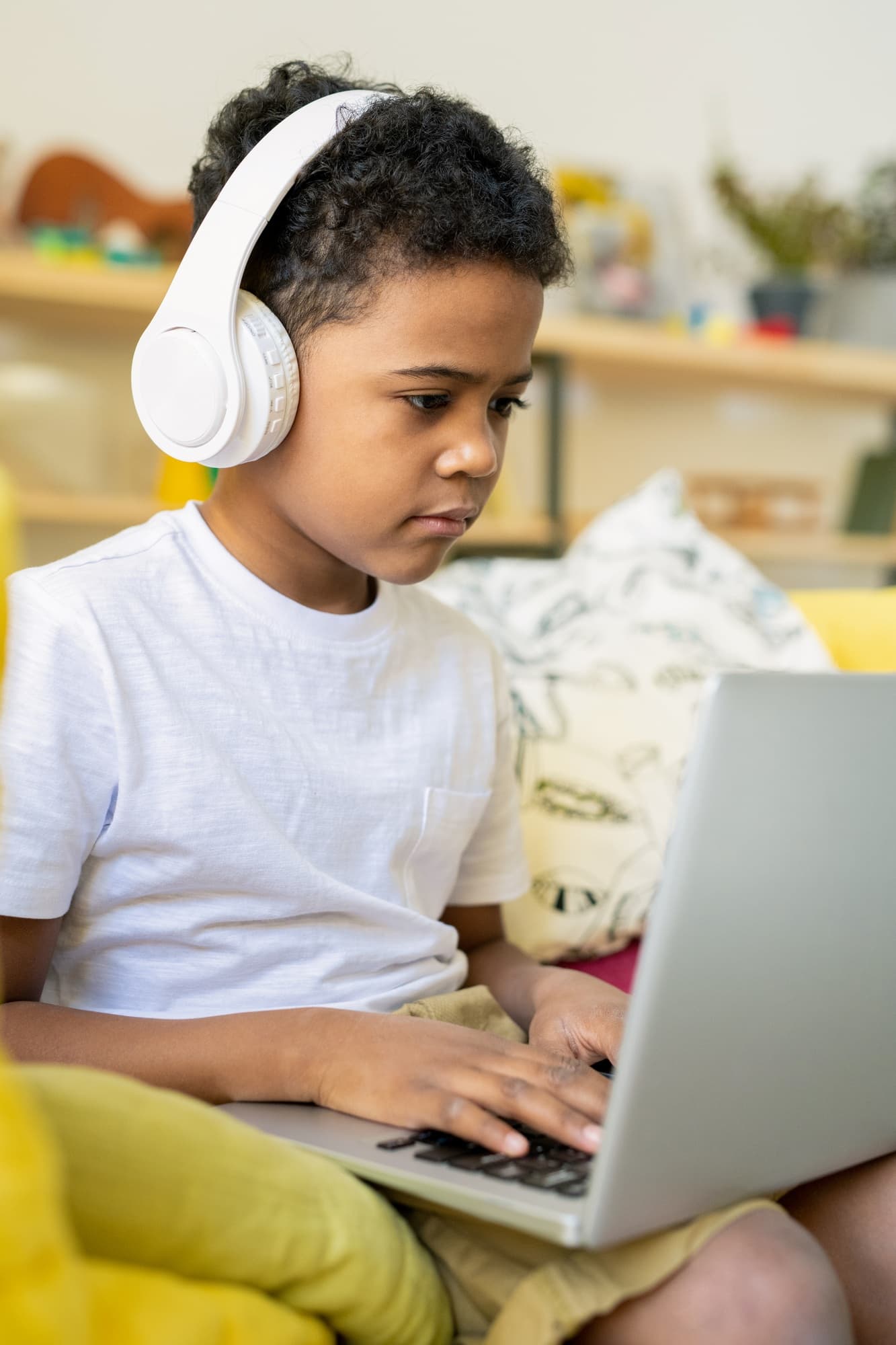 Elementary schoolboy with headphones typing on a laptop